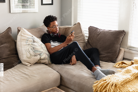 Black teen boy on phone at home on couch, cozy