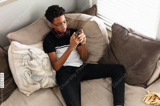 Black teen boy on phone at home on couch, cozy