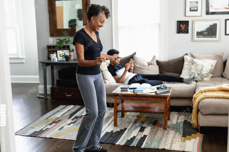 Black mom enjoys music, dancing in family room, son in background, weekend morning