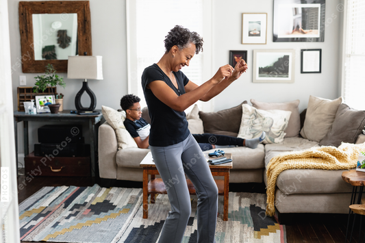 Black mom enjoys music, dancing in family room, son in background, weekend morning