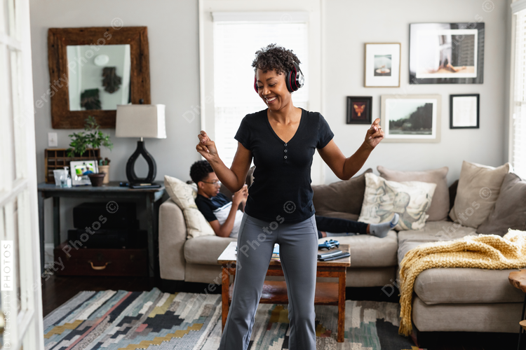 Black mom enjoys music, dancing in family room, son in background, weekend morning