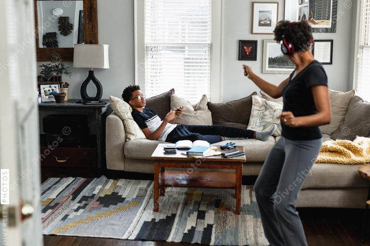 Black mom enjoys music, dancing in family room, son in background, weekend morning