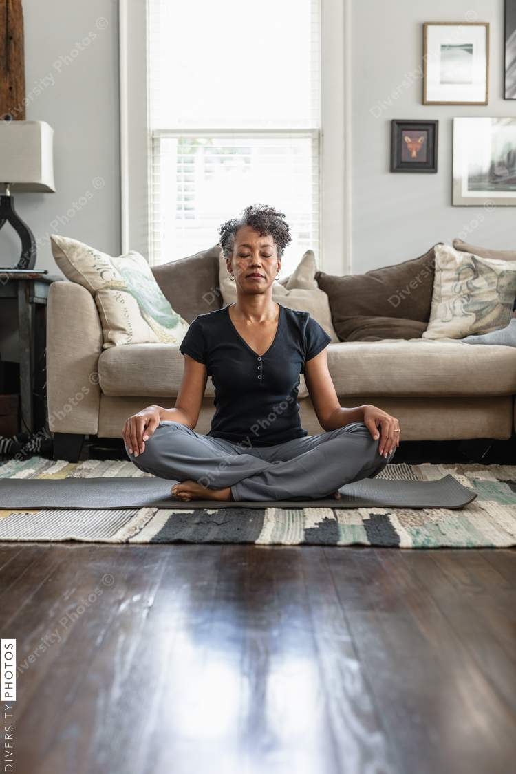 Black mom meditates in family room, teenage son on phone in background, peaceful health  and wellness