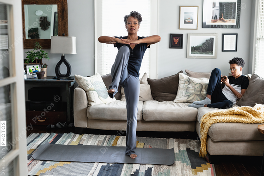 African American woman exercising in family room at home, teen son in background