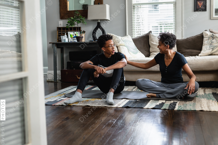 Teen son and mother talking in family room on yoga mat