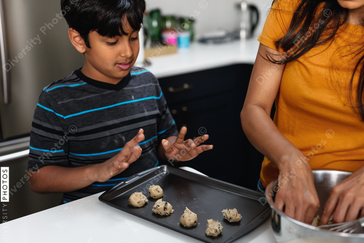 Indian mother and son preparing homemade treats in kitchen