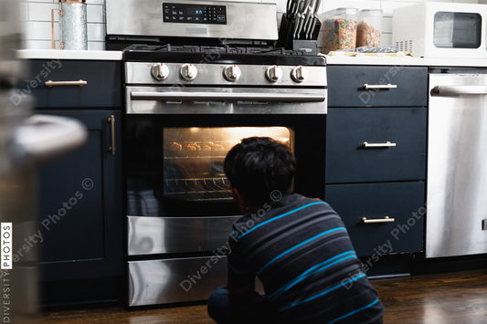 Young Indian boy waits for homemade cookies to bake in the oven