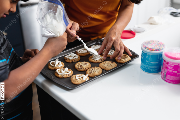 Indian mother and son decorating fresh baked cookies in the kitchen