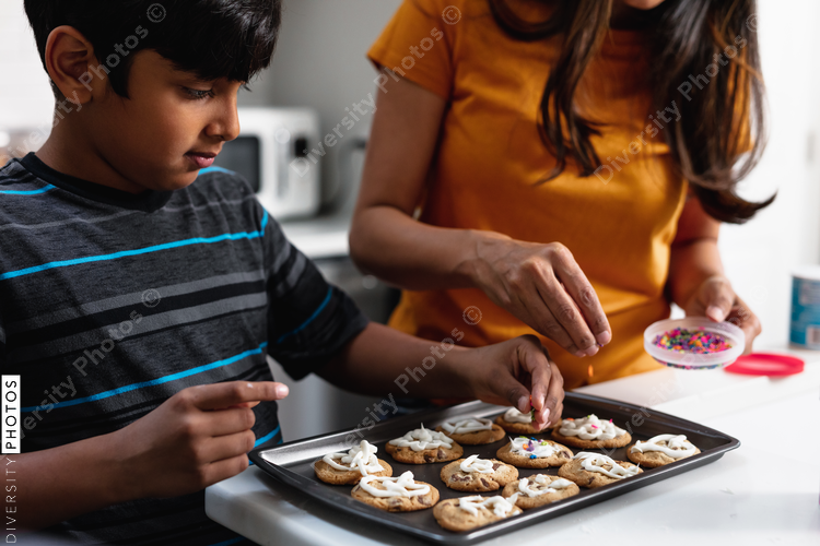 Indian mother and son decorating fresh baked cookies in the kitchen