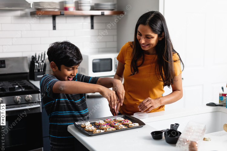 Indian mother and son decorating fresh baked cookies in the kitchen