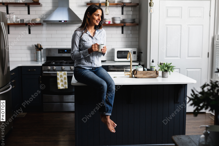Young Indian woman sitting on kitchen counter, with tea drink