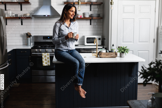 Young Indian woman sitting on kitchen counter, with tea drink