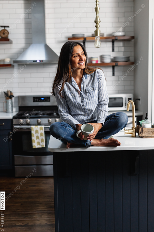 Young Indian woman sitting on kitchen counter, with tea drink