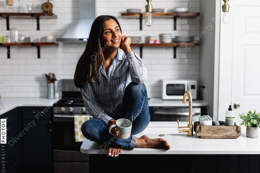 Young Indian woman sitting on kitchen counter, with tea drink