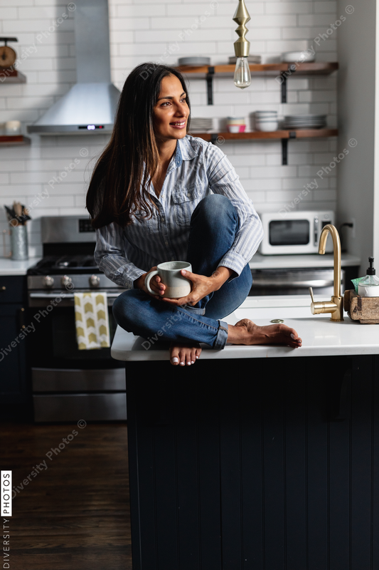 Young Indian woman sitting on kitchen counter, with tea drink