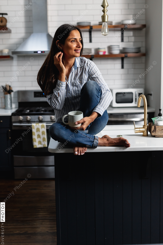 Young Indian woman sitting on kitchen counter, with tea drink