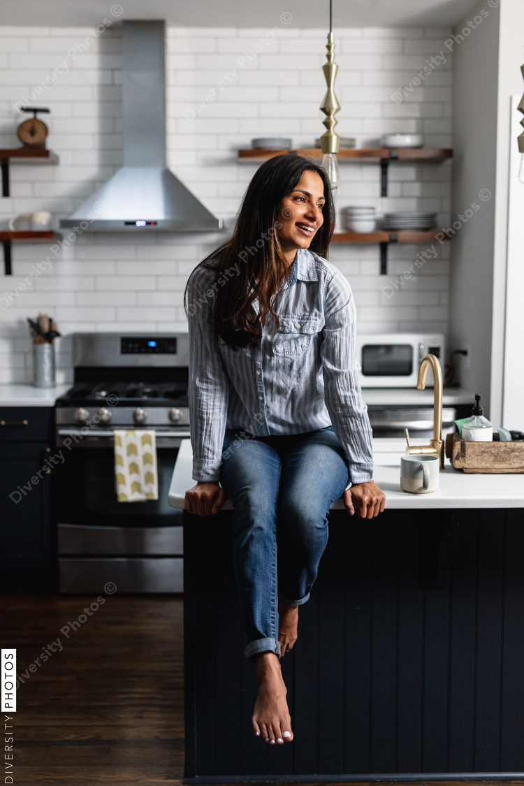 Young Indian woman sitting on kitchen counter