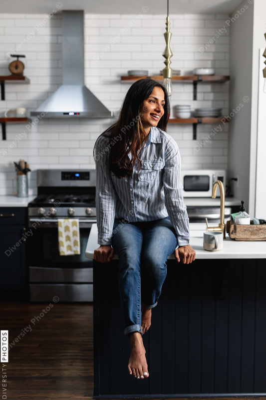 Young Indian woman sitting on kitchen counter