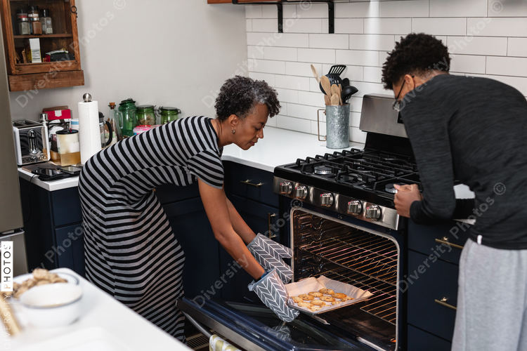 Mom pulls fresh baked cookies from the oven while son watches anxiously