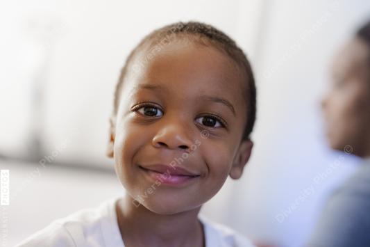 Young Black boy toddler smiling with mother in background, blurred, handsome