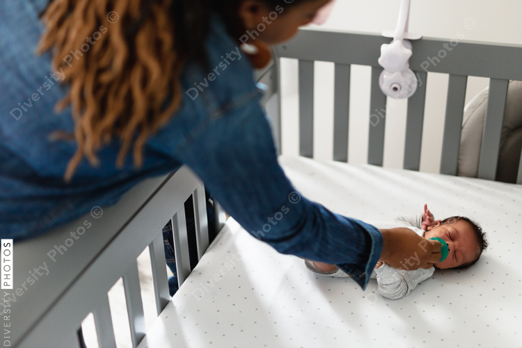 Black mom checking on crying baby in crib