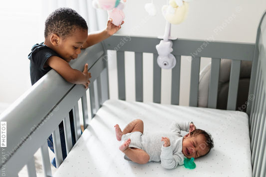 Big brother checking on sibling in crib, crying baby