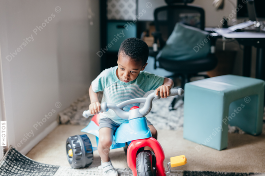Black boy riding on toy tricycle 