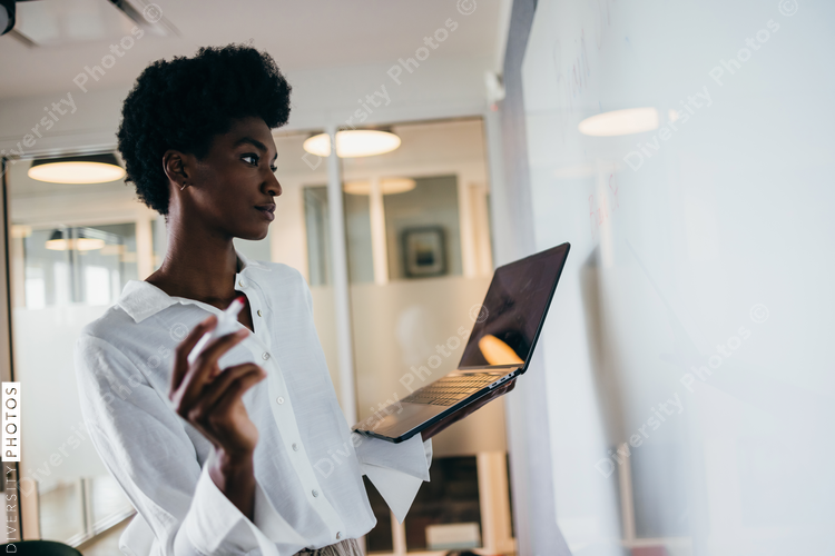 Focused Black businesswoman with laptop brainstorming on whiteboard