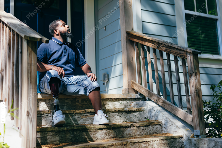 Black man with prosthetic leg sitting at front porch of new home purchase