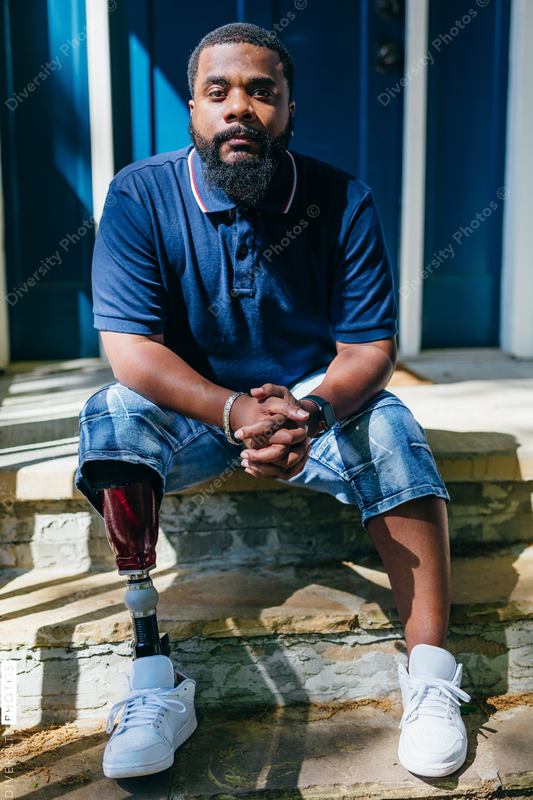 Black man with prosthetic leg sitting at front porch of new home purchase