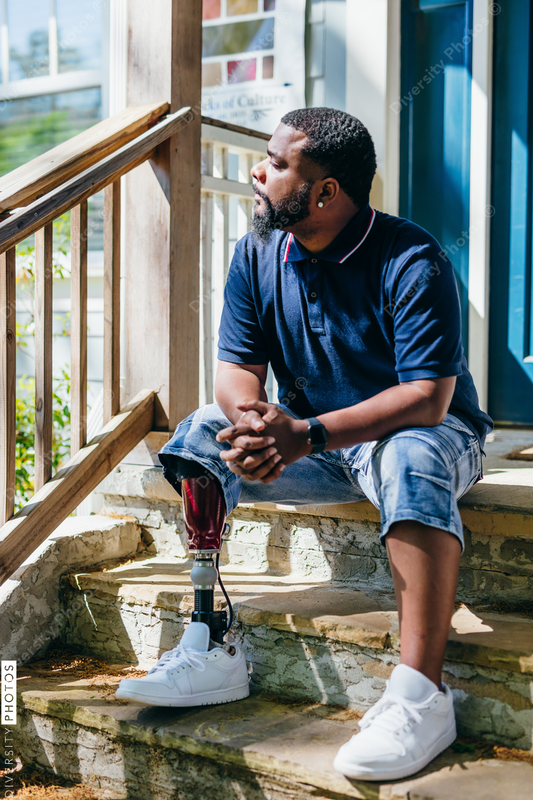 Black man with prosthetic leg sitting at front porch of new home purchase