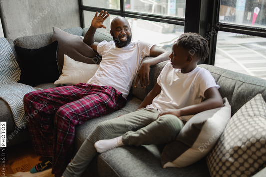 Black Father and son sitting on sofa in living room