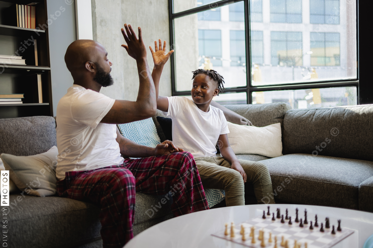 African American Father and son sitting on sofa in living room, giving high five