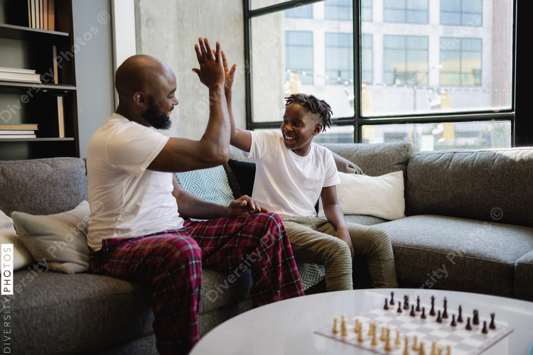 Black Father and son sitting on sofa in living room, giving high five
