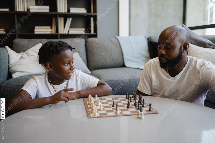 Black Father and son playing chess in living room
