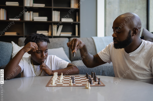 Black Father and son playing chess in living room
