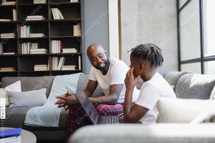 Father and son with laptop sitting on sofa in living room