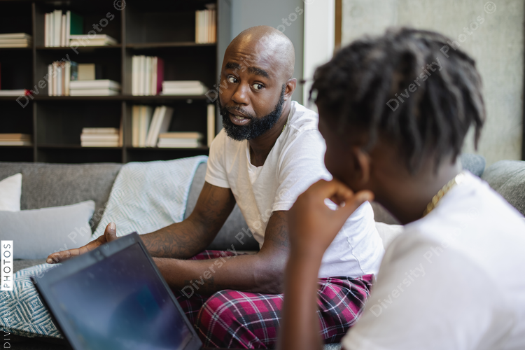 Father and son with laptop sitting on sofa in living room