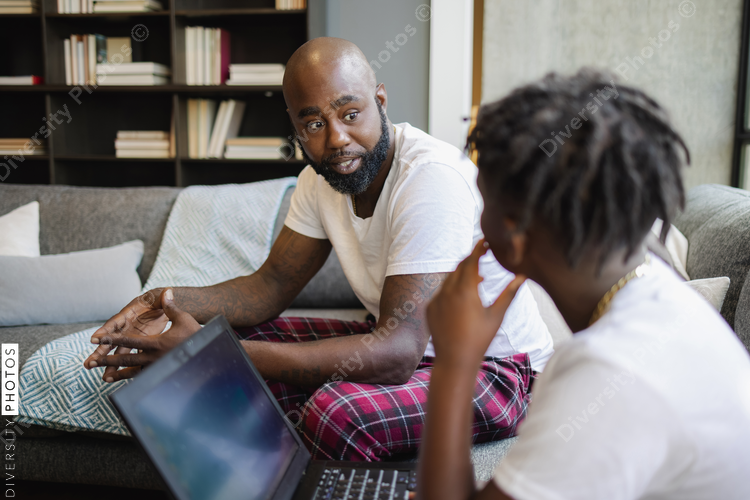 Father and son with laptop sitting on sofa in living room