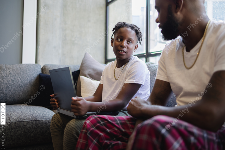Father and son with laptop sitting on sofa in living room