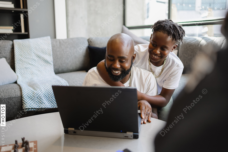 Affectionate son hugging father working at laptop in living room