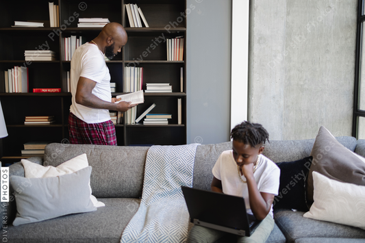 Black Boy using laptop on sofa in living room, father at bookshelf in background