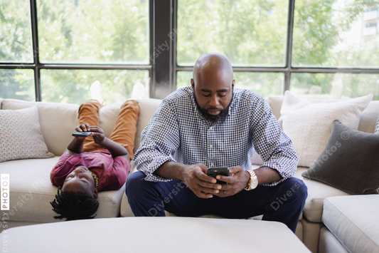 Black Father and son using smart phones on sofa