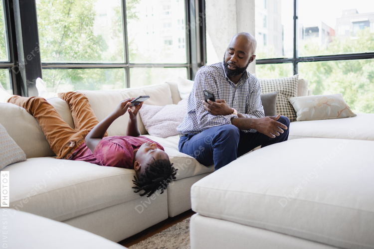 Black Father and son using smart phones on sofa