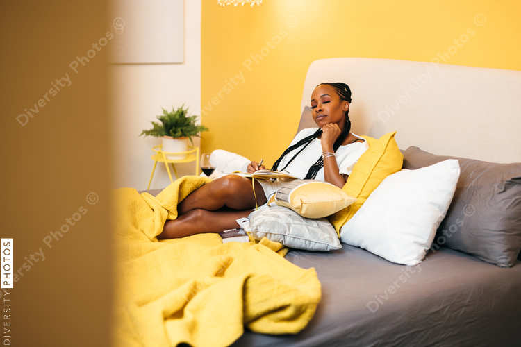 Black woman writes in journal at home in bed