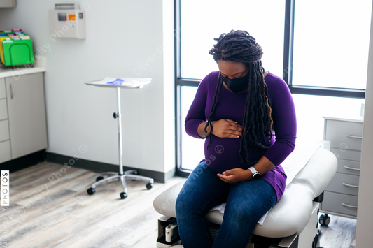Black pregnant woman waiting in medical exam room at the Doctors office, wearing mask