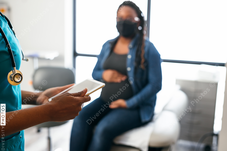 Black nurse speaking with female patient, holding digital tablet 