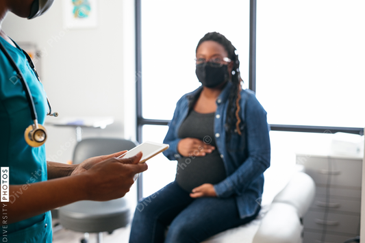 Black nurse speaking with female patient, holding digital tablet 