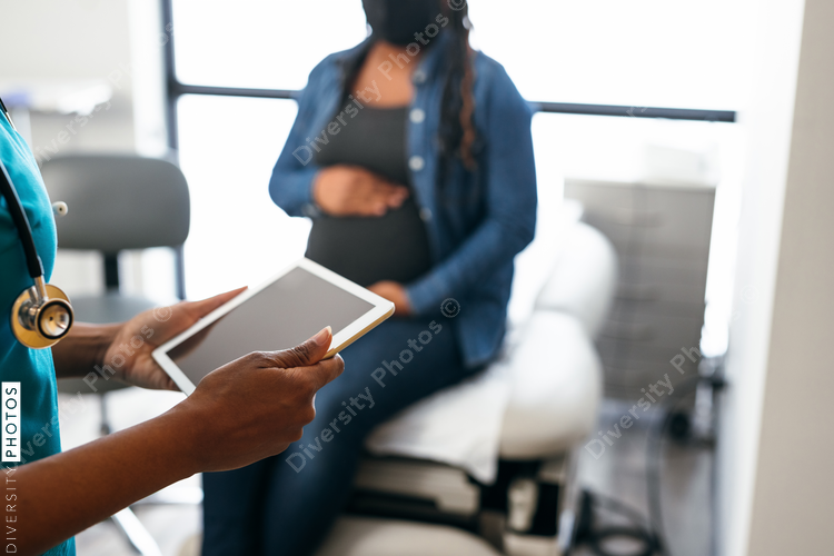 Black nurse speaking with female patient, holding digital tablet 