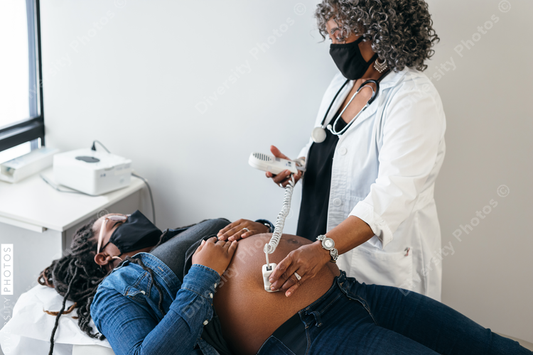 Black female senior doctor listening to fetal heartbeat, using a doppler sonogram, connection, wearing a mask